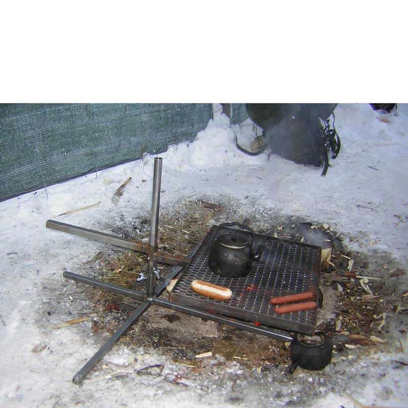 Ett höj och sänkbart grillgaller är monterat på en kryssfot och ställd på den snötäckta marken. Under gallret brinner en eld och på gallret grillas korv och kokas kaffe. Fikapaus under renskiljning,