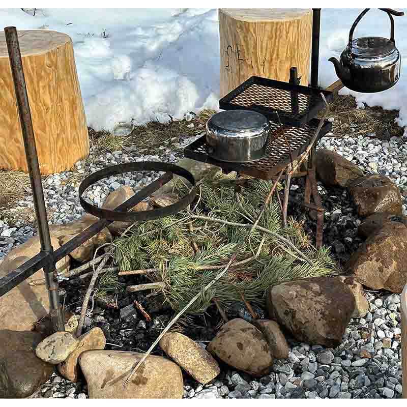 En eldstad på en grusbädd på marken. Två markrör är nedslagna i marken. På det ena är en stekhällsring monterad. På det andra röret är ett grillgaller 30x40, en kaffekrok med kaffepanna samt en varmhållningshylla monterad.